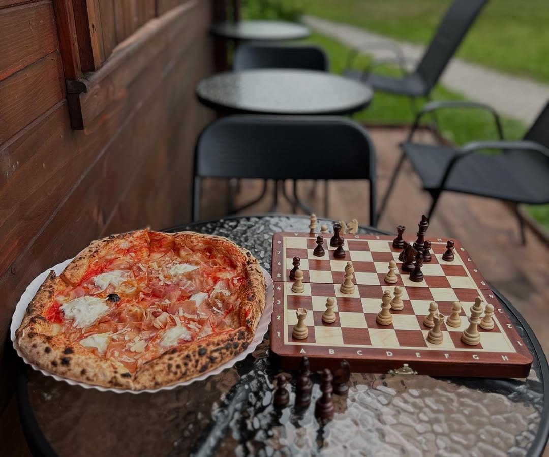 Pizza neapolitańska we wnętrzu pizzerii Fratelli Polacchi w Garwolinie Pizza neapolitańska na stole obok szachownicy we wnętrzu pizzerii Fratelli Polacchi w Garwolinie